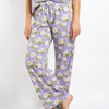 A person wearing lavender pajama pants with a white, green, and yellow floral print, paired with a matching top, shown against a plain white studio background.