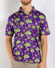 A man wearing a purple short-sleeve button-up shirt with a colorful Mardi Gras pattern featuring green trees, masks, beads, and ladders, paired with khaki pants against a light gray background.