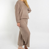 A woman modeling a matching two-piece lounge set in a soft, fuzzy taupe-brown fabric, consisting of a long-sleeve cropped sweater and wide-leg pants, against a plain white studio background.