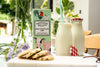 Box of Farmhouse Biscuits, cookies, and milk bottles on a table with flowers.